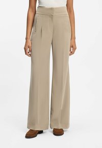 Wijde, beige broek van gladde stof. Heeft een hoge taille met voorplooien en zijzakken. Details zijn onder andere geplooide zoom.