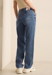 Pantaloni in corda azzurri chiari con fit dritto, caratterizzati da tasche posteriori e un'etichetta tessuta sulla vita. Indossati con sneakers bianche.