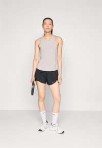 Vaaleanharmaa urheilutanktoppi ja mustat shortsit, kädessä painolautanen. Valkoiset urheilikengät ja sukat, joissa on musta Nike-logo, yksinkertainen muotoilu.