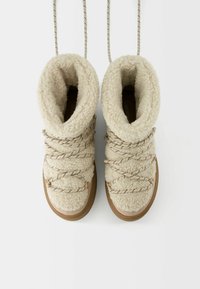 Beige, plysede støvler med en høj, blød krave, der har krydsede snørebånd og en tekstureret overdel. Brune gummisåler giver godt greb.