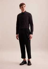 Zwart overhemd met knopen en lange mouwen, gecombineerd met zwarte, op maat gemaakte broek en zwarte nette schoenen. Gladde stof en een aansluitend ontwerp.