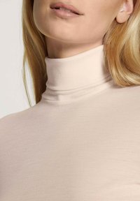 Light beige turtleneck made from soft, stretchable fabric; features a high collar and a smooth texture.