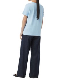 Hellblaues T-Shirt mit kurzen Ärmeln aus weichem Material, kombiniert mit dunkelblauen weit geschnittenen Jeans, von hinten gezeigt. Schwarze Schuhe werden getragen.