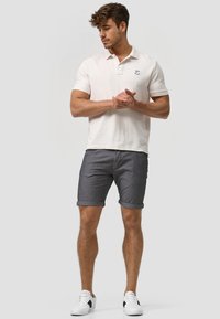 Polo shirt blanc à manches courtes, shorts gris à revers, et baskets blanches avec des accents noirs. Conception classique avec un détail de logo sur le polo.