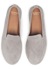 Zapatos slip-on de ante gris con acentos de costura y una textura suave. El interior presenta un forro de cuero marrón. El nombre de la marca es visible en la plantilla.
