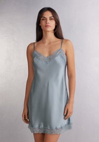 Jasnoniebieska satynowa sukienka na ramiączkach z koronkowym wykończeniem dekoltu i hemu. Posiada cienkie, regulowane ramiączka oraz gładką, błyszczącą teksturę.