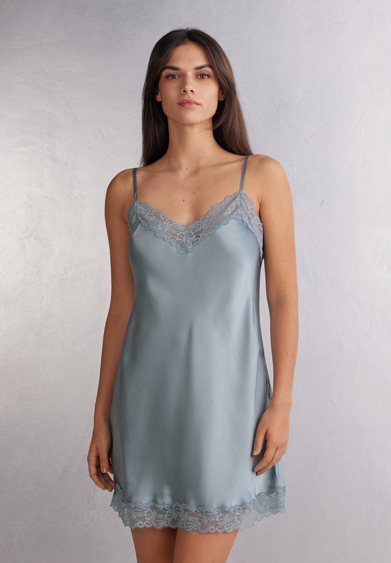 Jasnoniebieska satynowa sukienka na ramiączkach z koronkowym wykończeniem dekoltu i hemu. Posiada cienkie, regulowane ramiączka oraz gładką, błyszczącą teksturę.