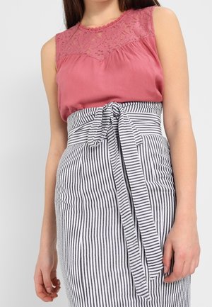 Kvinde iført ærmeløs lyserød blonder top og sort-hvid stribet nederdel med højtaljet og et bundet bælte i taljen.