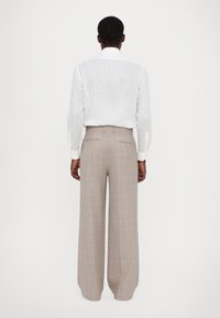 Camicia bianca di lino con maniche lunghe, abbinata a pantaloni grigi a quadri a vita alta e gamba larga, con strisce rosa e tasche posteriori.