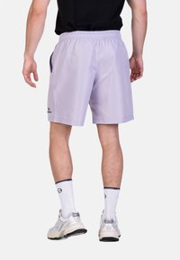 Shorts sportivi di un leggero colore lavanda realizzati in materiale leggero, dotati di un cinturino elastico e tasche laterali, indossati con calze bianche e sneakers.