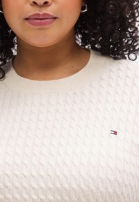 Εκρού πουλόβερ με πλέξη καλώδιο, ριμπ λαιμόκοψη και μικρό κεντητό λογότυπο σε κόκκινο, λευκό και μπλε στο τελείωμα, με υφή σχεδίου.