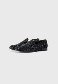 Pair of black slip-on shoes with textured, shiny stone embellishments on a clean white background.