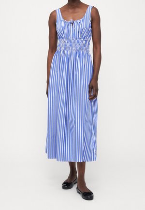 Gestreiftes Midikleid in Blau und Weiß, mit gerafftem Bund, runder Ausschnitt und breiten Trägern. Getragen mit schwarzen flachen Schuhen.