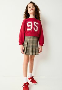 Rød cropped sweatshirt med hvid "95" print, parret med en ternet A-line nederdel. Modellen har røde sneakers og hvide ankelsokker på.