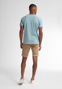Light blue short-sleeve t-shirt with a textured pattern, paired with khaki rolled-cuff shorts and white sneakers featuring a tan accent.