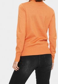 Orange stickad tröja med rund halsringning, ribbade ärmslut och nederkant, parat med mörka slim-fit jeans. Slät textur, figurnära design.