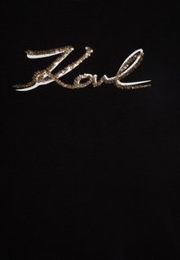 Μαύρο βαμβακερό t-shirt με λευκή και χρυσή κεντημένη γραφή. Το μπλουζάκι έχει κοντά μανίκια και στρογγυλή λαιμόκοψη.