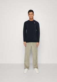 Marineblauwe longsleeve sweatshirt met geribbelde manchetten en zoom, voorzien van een klein logo op de borst, gecombineerd met lichtbeige corduroy broek.