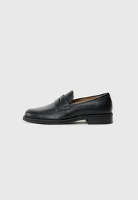 Black leather loafers with a rounded toe, featuring a front strap detail and a low, solid heel. Smooth texture and sleek design.