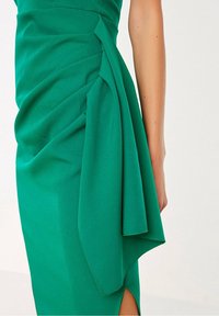 Grön klänning med draperad tyg på sidan, mjukt material och en något asymmetrisk fåll med en högt skärning.