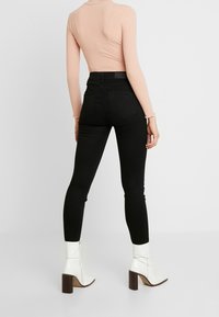 Jeans ajustados de tiro alto en negro, con una textura suave y costuras mínimas, combinados con botines blancos de tobillo con tacón cuadrado y detalle de cremallera.