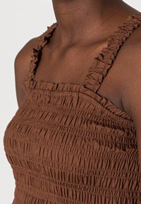 Haut smocké marron avec bretelles à volants et tissu texturé à détails froncés, conçu pour une silhouette ajustée.