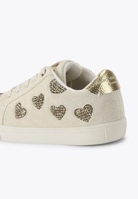 Zamszowe tenisówki w jasnym beżu z ozdobami w kształcie złotego serca. Teksturalne złote akcenty na pięcie, zakończone białą podeszwą.