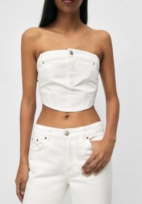 Haut court en denim blanc avec un design sans bretelles, présentant des coutures frontales et un bouton argenté en guise d'accent. Associé à un pantalon en denim blanc.