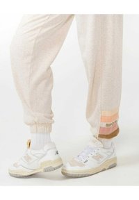 Ljusbeige joggers med elastiska mudd och en flerfärgad randig detalj vid fållen. Bärs med vita sneakers med grå accenter.