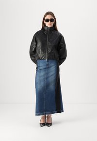Veste bomber en cuir noir, col haut, fermeture éclair à l'avant. Jupe en denim longue avec sections bleues et noires, ourlet effiloché. Escarpins noirs.