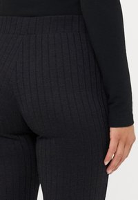 Fekete, bordázott leggings, magas derékkal. Az anyag textúrázott mintázattal és sima felülettel rendelkezik, kiemelve a formát.