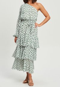 Vestido con estampado floral de un solo hombro, tejido blanco con patrones verdes, volantes en capas y un cinturón a juego.