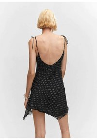 Robe sans manches noire avec un motif à pois, bretelles réglables et dos décolleté. Tissu fluide avec un ourlet asymétrique.