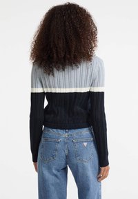 Maglione a costine nei colori grigio, bianco e blu navy; design aderente con maniche lunghe e orlo corto, abbinato a jeans blu a vita alta.