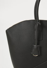 Black leather tote bag with a textured surface, rounded top, and a zip closure. Features a leather strap and subtle gold hardware.
