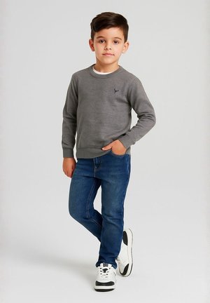 Grå tröja med rundad krage och ribbade ärmslut, tillsammans med blå denimjeans. Vita och svarta sneakers med texturerade detaljer.