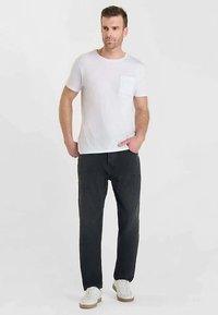 T-shirt en coton blanc avec poche poitrine, associé à un jean en denim noir, porté avec des baskets blanches à semelles beiges.