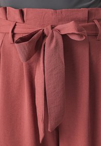 Rust-colored wide-leg pants with a textured fabric, featuring a tied waistband and pleated detailing at the top.