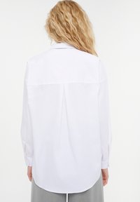 White shirt with long sleeves and a back pleat. Designed with a classic collar and button details on the cuffs, made of lightweight fabric.