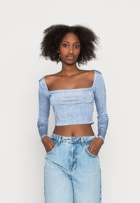 Top cropped azul de manga longa com decote reto e padrão de espinha de peixe texturizado, combinado com jeans claros de cintura alta.