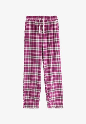 Jeune femme debout portant un t-shirt violet, un pantalon à carreaux rose et blanc, et des chaussons blancs sur un fond blanc uni.
