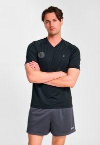 Svart atletisk t-shirt med V-ringning, korta ärmar och en logotyp på vänster bröst. Kombinerad med gråa meshshorts med en subtil design.