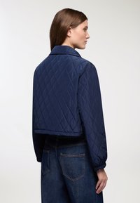 Giacca trapuntata blu navy con colletto, dal design cropped e polsi elasticizzati, caratterizzata da una texture liscia e un motivo a diamante.