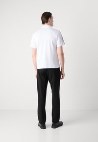 Balta trumpo rankovų polo marškinėliai su apykakle, derinami su juodomis kelnėmis. Apranga pasižymi lygiu audiniu ir paprastu dizainu.