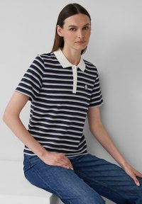 Navy en witte gestreepte poloshirt met een crèmekleurige kraag en vier knopen, voorzien van een rond geborduurd logo op de borst.