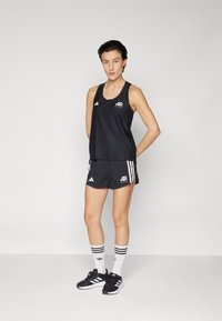 Black athletic tank top and shorts with white accents, featuring side stripes. Worn with black sneakers and knee-high white socks with stripes.