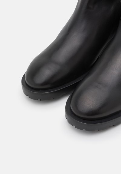 Bottines en cuir noir à bout rond, avec une surface texturée et une épaisse semelle en caoutchouc noir présentant un motif de bande de roulement robuste.