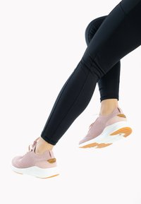Světle růžové pletené tenisky s bílou podrážkou a oranžovými akcenty, styled s černými legínami, s prodyšnou texturou a šněrováním.
