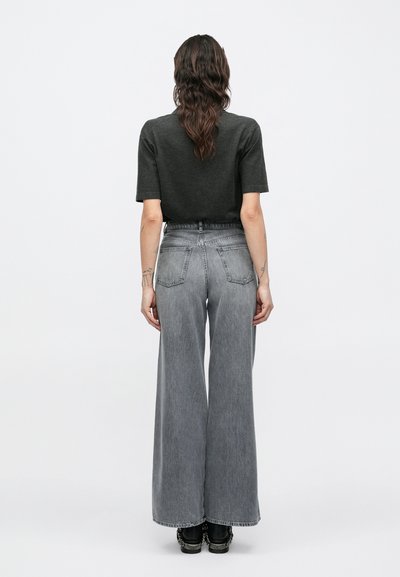 Jean gris à jambes larges avec une taille haute, doté de poches arrière et d'une finition délavée, associé à un haut sombre à manches courtes.