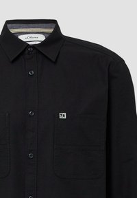 Schwarzes Hemd mit Knöpfen und spitzem Kragen, zwei Brusttaschen und subtiler Markenlogo. Hergestellt aus einem glatten, strukturierten Stoff. Reguläre Passform.